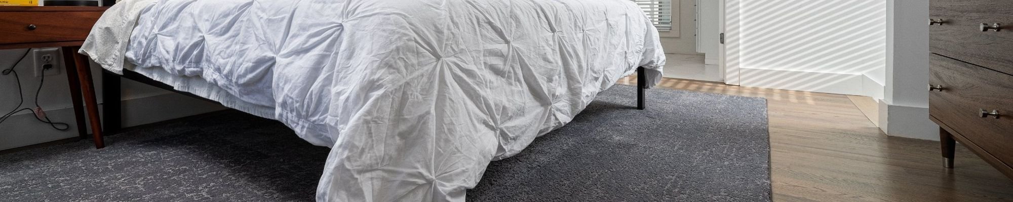 bed with white duvet on dark grey area rug - Carpet Plus Flooring LLC